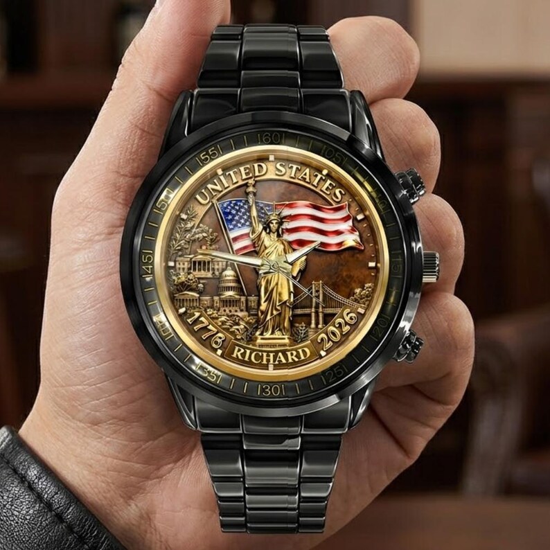 May include: Black wristwatch with a detailed face featuring the Statue of Liberty, the American flag, and the text "UNITED STATES" and "RICHARD". The watch has a black metal band and a gold-colored bezel.