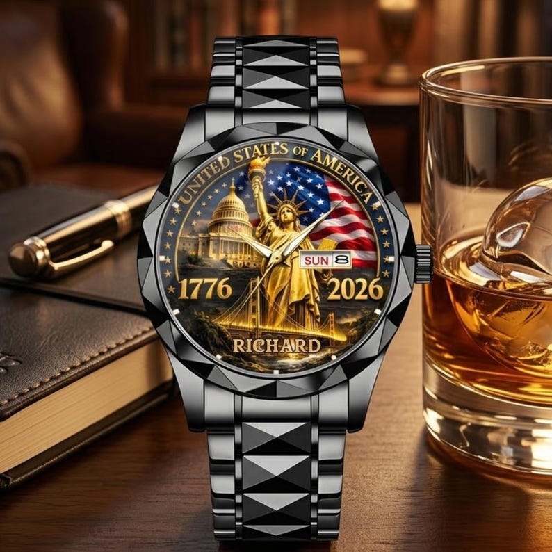 May include: A black wristwatch with a detailed face featuring the Statue of Liberty, the U.S. Capitol, and the American flag. The watch face includes the text "UNITED STATES OF AMERICA", "1776", and "2026". The watch band is a geometric design.