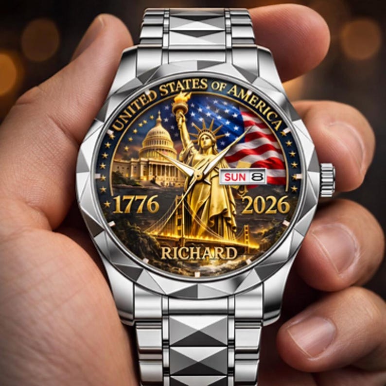 May include: A silver wristwatch with a detailed face featuring the Statue of Liberty, the U.S. Capitol, and an American flag. The watch face includes the text "UNITED STATES OF AMERICA", "1776", "2026", and "RICHARD". The watch band is made of silver links.