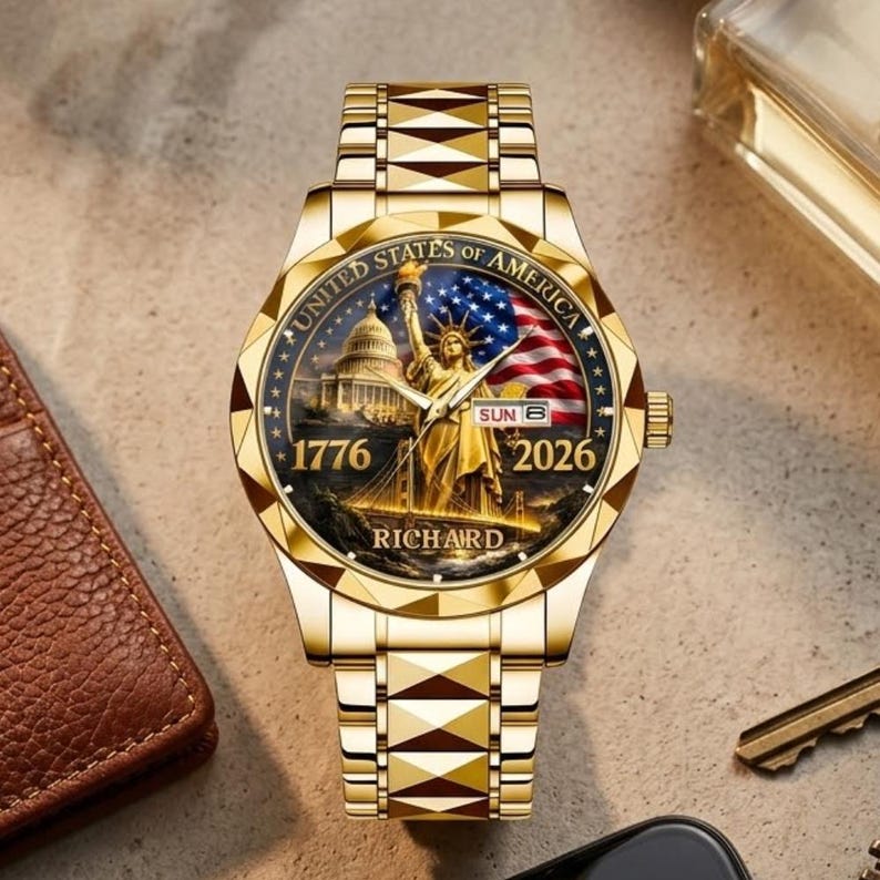 May include: Gold-coloured wristwatch with a detailed face depicting the Statue of Liberty, the American flag, and the Capitol building. The watch face includes the text "UNITED STATES OF AMERICA", "1776", "2026", and "RICHARD". The watch band has a geometric design.
