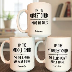 May include: Three white ceramic mugs with black text. The mugs read "I'M THE OLDEST CHILD I MAKE THE RULES", "I'M THE MIDDLE CHILD I'M THE REASON WE HAVE RULES", and "I'M THE YOUNGEST CHILD THE RULES DON'T APPLY TO ME".