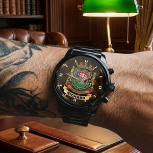 May include: Black wristwatch with a custom face featuring a coat of arms design and the name "RICHARD". The watch has a black metal band and a dark face. The watch is on a person's wrist.