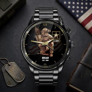 Puede incluir: Reloj de pulsera negro con una esfera detallada que presenta un soldado, el logotipo del ej&eacute;rcito estadounidense y un dise&ntilde;o de la bandera estadounidense. El reloj tiene una correa de metal negro y el nombre "BRIAN" y el a&ntilde;o "EST. 1988" est&aacute;n impresos en la esfera.