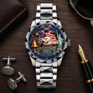 May include: A silver-tone wristwatch with a blue dial featuring a bald eagle, the Statue of Liberty, a bell, and an American flag. The dial displays the text JAMES, UNITED STATES OF AMERICA, 250th ANNIVERSARY, 1776-2026, and SUN 8.