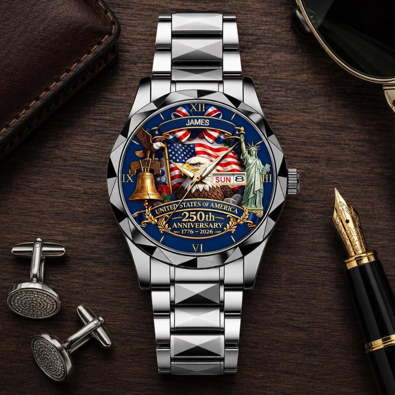 May include: A silver-tone wristwatch with a blue dial featuring a bald eagle, the Statue of Liberty, a bell, and an American flag. The dial displays the text JAMES, UNITED STATES OF AMERICA, 250th ANNIVERSARY, 1776-2026, and SUN 8.
