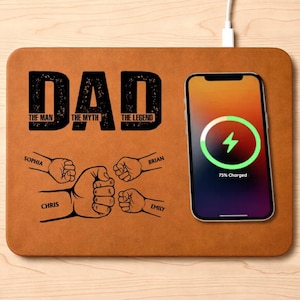 May include: A brown wireless charging pad with the word "DAD" in large black letters. Below, it reads "The Man, The Myth, The Legend." The pad features fist bump illustrations with names. A phone displays a charging symbol.