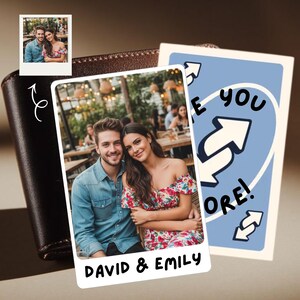 Peut inclure: Un portefeuille en cuir marron avec une photo d'un couple et une carte bleue avec l'inscription "I love you more!". La photo est une impression de style Polaroid avec les noms "David & Emily".