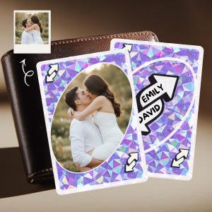 Puede incluir: Dos cartas de Uno personalizadas con una pareja besándose, con los nombres "Emily" y "David" en una carta. Las cartas tienen un diseño geométrico morado y blanco. Una pequeña foto de la pareja está en la esquina y una cartera de cuero marrón está en el fondo.