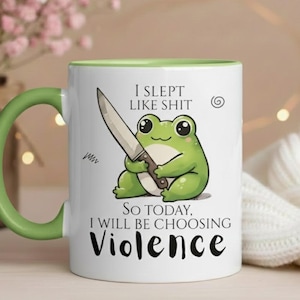 May include: White ceramic mug with a green handle and rim. The mug features a cartoon frog holding a knife, with the text "I SLEPT LIKE SHIT. SO TODAY, I WILL BE CHOOSING VIOLENCE."