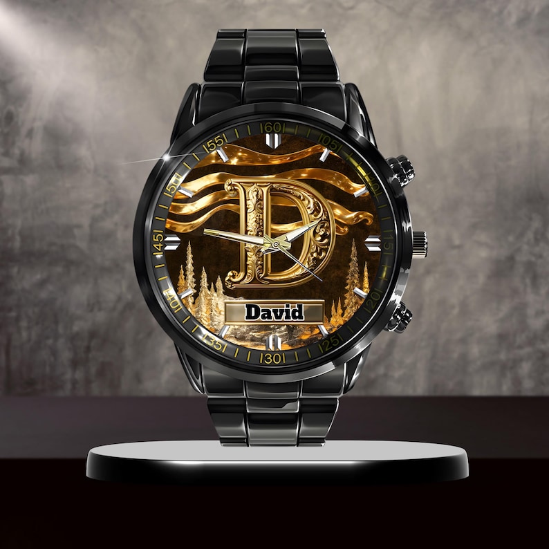 K&ouml;nnte beinhalten: Schwarze Armbanduhr mit goldenem Zifferblatt, das den Buchstaben "D" und den Namen "David" zeigt. Die Uhr hat ein schwarzes Metallarmband und ein rundes Zifferblatt mit goldenen Akzenten und einer Waldszene.