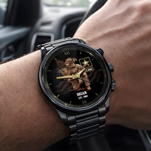 Puede incluir: Reloj de pulsera negro con una correa de metal negro. La esfera del reloj presenta un gr&aacute;fico de un soldado, el logotipo del Ej&eacute;rcito de EE. UU. y el texto "BRIAN EST. 1988". Las manecillas del reloj son doradas.