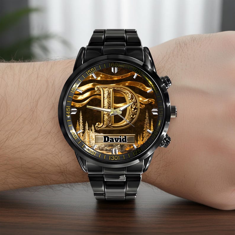 K&ouml;nnte beinhalten: Schwarze Armbanduhr mit goldenem Zifferblatt, das den Buchstaben "D" und den Namen "David" zeigt. Die Uhr hat ein schwarzes Metallarmband und eine goldfarbene L&uuml;nette mit Zahlen. Die Uhr befindet sich an einem Handgelenk.