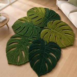 May include: A large area rug shaped like a cluster of overlapping monstera leaves in various shades of green, ranging from light lime to deep forest green. The rug features a textured, tufted surface with cutouts mimicking the natural leaf veins.