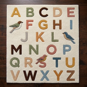 May include: A rectangular off-white area rug featuring the English alphabet in raised, multi-coloured letters. The design includes three small bird illustrations positioned near the letters F, J, and S, with each letter rendered in a distinct muted tone.