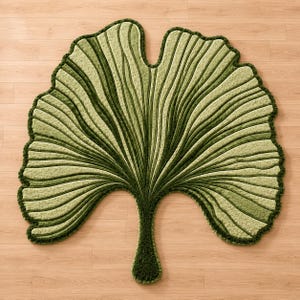 Pode incluir: Um tapete grande em forma de folha com uma superf&iacute;cie texturizada em tons de verde claro e escuro. O design imita uma folha de ginkgo com veios proeminentes e elevados que irradiam da base at&eacute; &agrave;s bordas recortadas, com um contorno verde escuro.