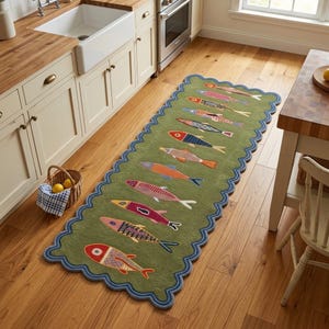 Peut inclure: Un long tapis de couloir rectangulaire aux bords festonnés vert olive, orné d'un motif répétitif de poissons stylisés de différentes couleurs, notamment rouge, rose, orange et bleu. Le tapis est posé sur un sol en bois dans une cuisine.