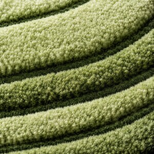 Pode incluir: Um tapete de pel&uacute;cia com uma superf&iacute;cie texturizada de pelo alto e faixas curvas alternadas de verde-lima claro e verde-floresta profundo. As fibras espessas e macias criam um padr&atilde;o ondulado em camadas por toda a superf&iacute;cie do tecido.
