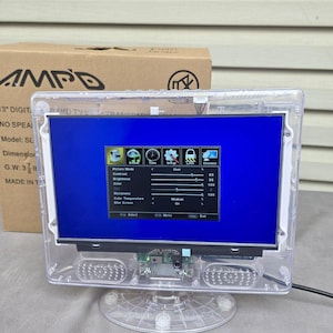 May include: A clear, transparent 7.6 cm digital display screen with a blue screen. The screen is mounted on a clear plastic stand. The screen displays a menu with picture mode, contrast, brightness, colour, sharpness, colour temperature, and blue screen options.