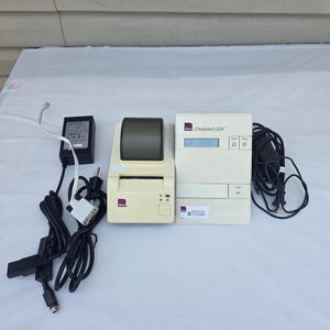 May include: An Alere Cholestech LDX diagnostic system in a cream-coloured casing, featuring a digital display, control buttons, and a label with technical support information. Includes a matching thermal printer, power cables, and data cords.