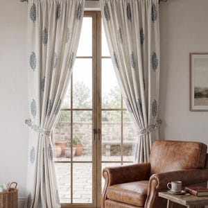May include: A pair of off-white floor-length curtains featuring a repeating blue paisley-style botanical print. The curtains are gathered and held back by matching fabric tiebacks, hanging from a simple rod over a tall glass-paned door.