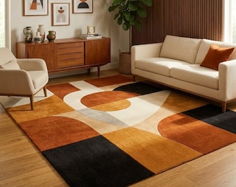May include: A rectangular area rug featuring a geometric pattern of large circles and blocks in shades of burnt orange, cream, and black. The rug is laid flat on a light-colored wooden floor, covering a significant portion of the visible floor space.
