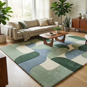 May include: A white ceramic mug with a black handle and the text "But First, Coffee" in a bold, black font. The mug is set against a blurred background, suggesting a cozy setting.