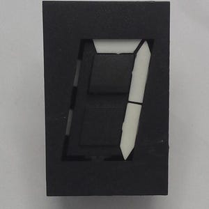 May include: A black, rectangular digital display showing the number seven. The number is formed by white, segmented lines against a black background. The display is likely for an electronic device.