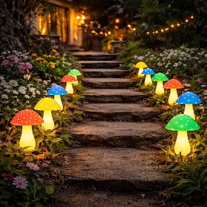 Puede incluir: Un sendero de jardín bordeado de luces con forma de hongo. Las luces tienen tapas de colores rojo, amarillo, azul y verde, con lunares blancos. El sendero conduce a una casa con iluminación cálida, creando una escena de jardín caprichosa.