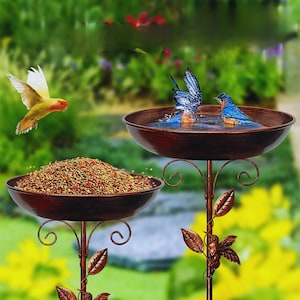 May include: A two-tiered bird feeder and bath set in a bronze finish. The upper tier contains water, with two blue birds bathing. The lower tier is filled with birdseed. A yellow and orange bird flies nearby. The metal stands feature leaf and swirl details.