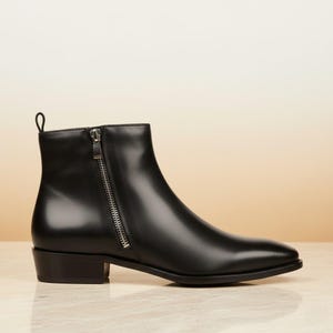May include: Black leather ankle boot with a side zipper and a small heel. The boot has a pointed toe and a pull tab at the back. The overall design is sleek and modern, suitable for various outfits.