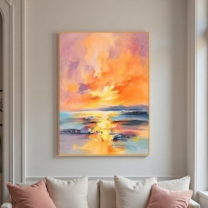 Può includere: Dipinto di paesaggio astratto con una vivace scena del tramonto. L'opera presenta una cornice dorata e raffigura un cielo colorato con sfumature di arancione, rosa e viola, che si riflettono sull'acqua sottostante. Il dipinto è esposto sopra un divano bianco con cuscini rosa.