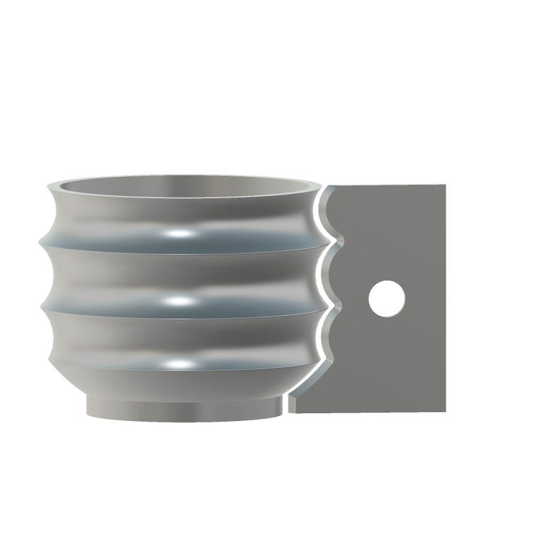 Puede incluir: Una taza de color gris met&aacute;lico con una superficie exterior ondulada y acanalada que presenta tres crestas horizontales redondeadas. En el lateral hay un asa rectangular plana con un borde festoneado y un orificio circular central.