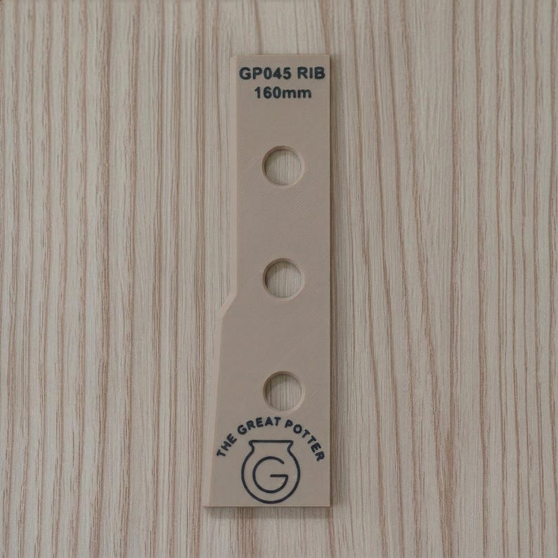 May include: A beige pottery rib tool with three circular holes and the text "GP045 RIB 160mm". The tool also features a logo that says "THE GREAT POTTER". The tool is set against a light wood grain background.