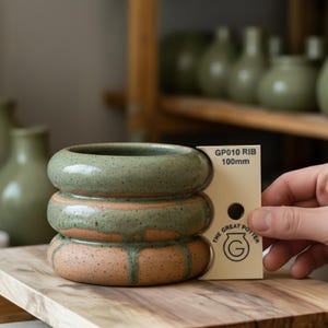 以下が含まれることがあります： 手作りのセラミックポット。積み重ねられたリング状のデザイン。 上部のリングは斑点のある緑色で釉薬が施され、自然なテラコッタ色のベースに釉薬が滴り落ちています。 ポットの直径は約10cmです。