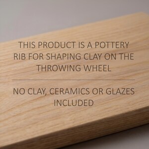 Puede incluir: Una costilla de madera rectangular para dar forma a la arcilla en el torno de alfarero. La superficie presenta el texto: THIS PRODUCT IS A POTTERY RIB FOR SHAPING CLAY ON THE THROWING WHEEL. NO CLAY, CERAMICS OR GLAZES INCLUDED. La madera tiene una veta clara.