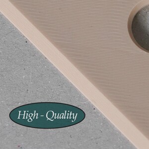 Puede incluir: Una tabla de madera de color beige claro con capas, una superficie lisa con l&iacute;neas diagonales y un recorte circular. Una pegatina ovalada de color verde azulado oscuro muestra el texto blanco "High-Quality" en fuente serif sobre un fondo gris.