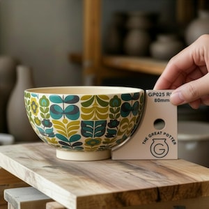 Könnte beinhalten: Eine Keramikschale mit cremefarbenem Boden und Innenraum, verziert mit einem Retro-Blumenmuster in Türkis, Grün und Gelb. Die Schale ist etwa 8 cm hoch, wie auf einer Messkarte angegeben. Das Logo The Great Potter ist sichtbar.