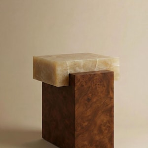 May include: A contemporary, two-tiered decorative stand. The base is a dark brown, rectangular block with a wood grain pattern. The top is a lighter, rectangular block with a marbled, beige appearance. A unique piece of home decor.