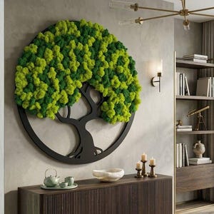 May include: A circular wall decoration with a tree design, framed in black. The tree's foliage is composed of green and yellow moss. The artwork is mounted on a light grey wall, bringing a natural element to the interior.