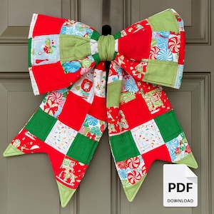 May include: A large, decorative Christmas bow made of red, green, and patterned fabric squares. The bow is attached to a door and features a central knot and pointed ends. The fabric has candy and holiday-themed designs.