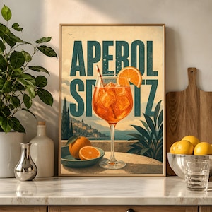 Puede incluir: Una l&aacute;mina decorativa rectangular con el texto APEROL SPRITZ en grandes letras verde oscuro. La ilustraci&oacute;n muestra una copa de tallo largo con un c&oacute;ctel naranja, cubitos de hielo y una rodaja de naranja frente a un paisaje costero.