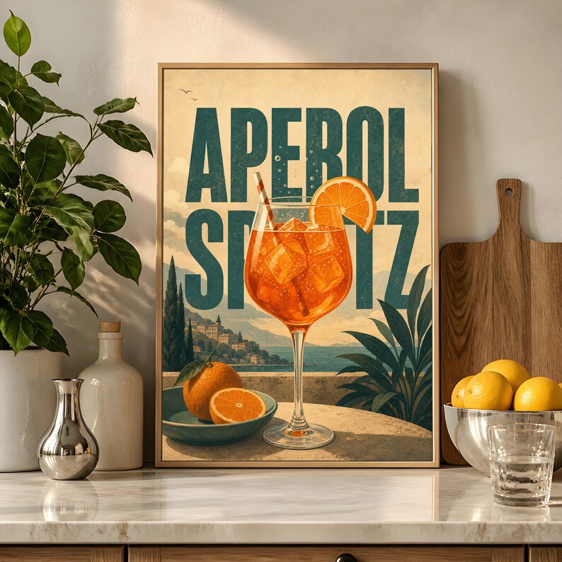Puede incluir: Una l&aacute;mina decorativa rectangular con el texto APEROL SPRITZ en grandes letras verde oscuro. La ilustraci&oacute;n muestra una copa de tallo largo con un c&oacute;ctel naranja, cubitos de hielo y una rodaja de naranja frente a un paisaje costero.