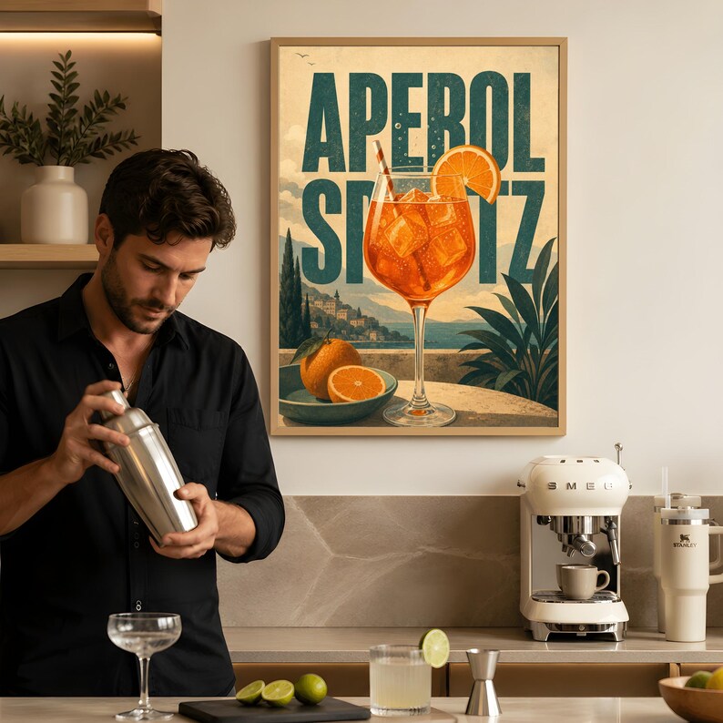 Puede incluir: Un cuadro decorativo enmarcado que muestra una ilustraci&oacute;n vibrante de un c&oacute;ctel Aperol Spritz en una copa con hielo y una rodaja de naranja, sobre un paisaje costero con el texto APEROL SPRITZ en letras grandes y llamativas.