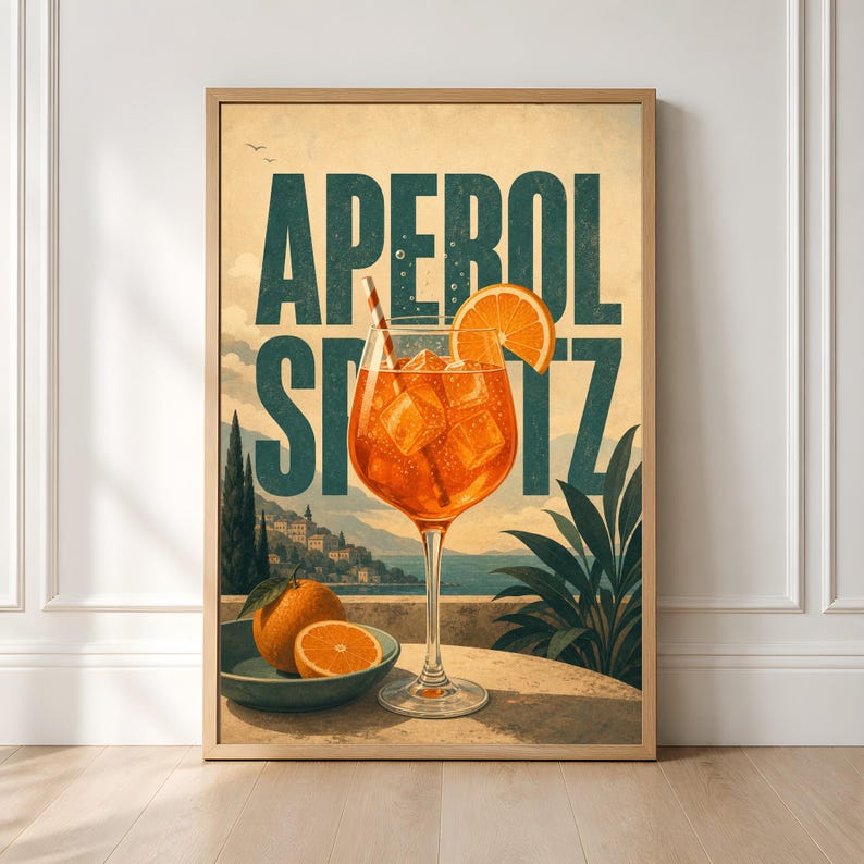 Puede incluir: Un p&oacute;ster enmarcado que muestra un c&oacute;ctel Aperol Spritz de color naranja vibrante en una copa con hielo y una pajita. El texto APEROL SPRITZ aparece en letras grandes de color verde oscuro. Un cuenco con naranjas enteras y cortadas descansa sobre una mesa.