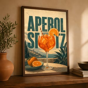 Puede incluir: Una l&aacute;mina enmarcada que muestra un vaso alto de Aperol Spritz naranja con cubitos de hielo y una pajita, sobre una mesa con naranjas frescas. El fondo muestra un paisaje costero con el texto APEROL SPRITZ en letras de color azul verdoso.