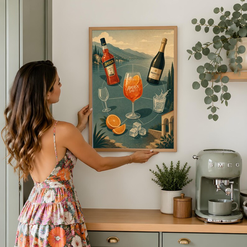 Może przedstawiać: Oprawiony wydruk ścienny z ilustracją koktajlu Aperol Spritz. Grafika przedstawia butelkę Aperolu, butelkę Prosecco, kieliszek Aperol Spritz, pustą szklankę, plasterki pomarańczy oraz kostki lodu na tle krajobrazu z jeziorem w tle.