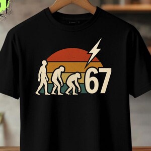 Può includere: T-shirt nero con un design retrò con il numero "67" e una grafica evolutiva. Il design include un tramonto nei toni dell'arancione, del rosso e del giallo, con un fulmine bianco. La maglietta ha anche il testo "ORIGINAL DESIGN" e "PNG DESIGN".