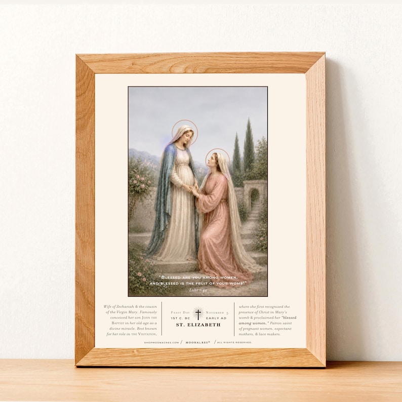 Puede incluir: Una impresi&oacute;n enmarcada que presenta una ilustraci&oacute;n religiosa de dos mujeres, una arrodillada y la otra de pie, ambas con halos. La mujer de pie lleva una capa azul y un vestido blanco, mientras que la mujer arrodillada lleva un vestido rosa. El marco es de madera clara.