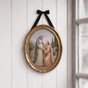 Puede incluir: Una impresi&oacute;n religiosa ovalada con marco dorado que representa a dos mujeres con t&uacute;nicas fluidas, una de ellas arrodillada. El marco es ornamentado y est&aacute; suspendido por una cinta negra atada con un lazo. La obra presenta colores suaves y un paisaje sereno.