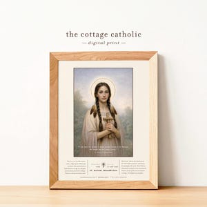 Puede incluir: Impresión digital enmarcada que presenta a Santa Kateri Tekakwitha. La imagen muestra a una joven con cabello largo y trenzado, sosteniendo una cruz. La impresión tiene un fondo claro y está enmarcada en madera natural. El texto superior dice "the cottage catholic - digital print -."